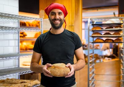 Corporate portrait of smiling bakery manager in the artisan bakery workshop, with a bread his hands Corporate portrait of smiling bakery manager in the artisan bakery workshop, with a bread his hands
